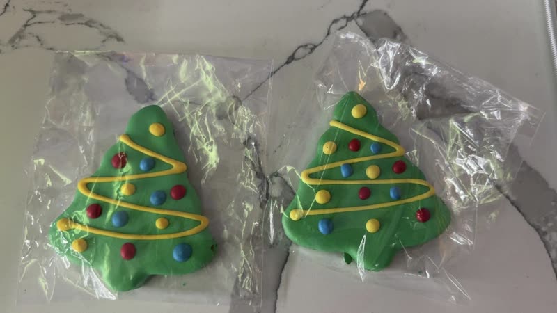 Two green Christmas-tree shaped dog biscuits in cellophane on a marble counter